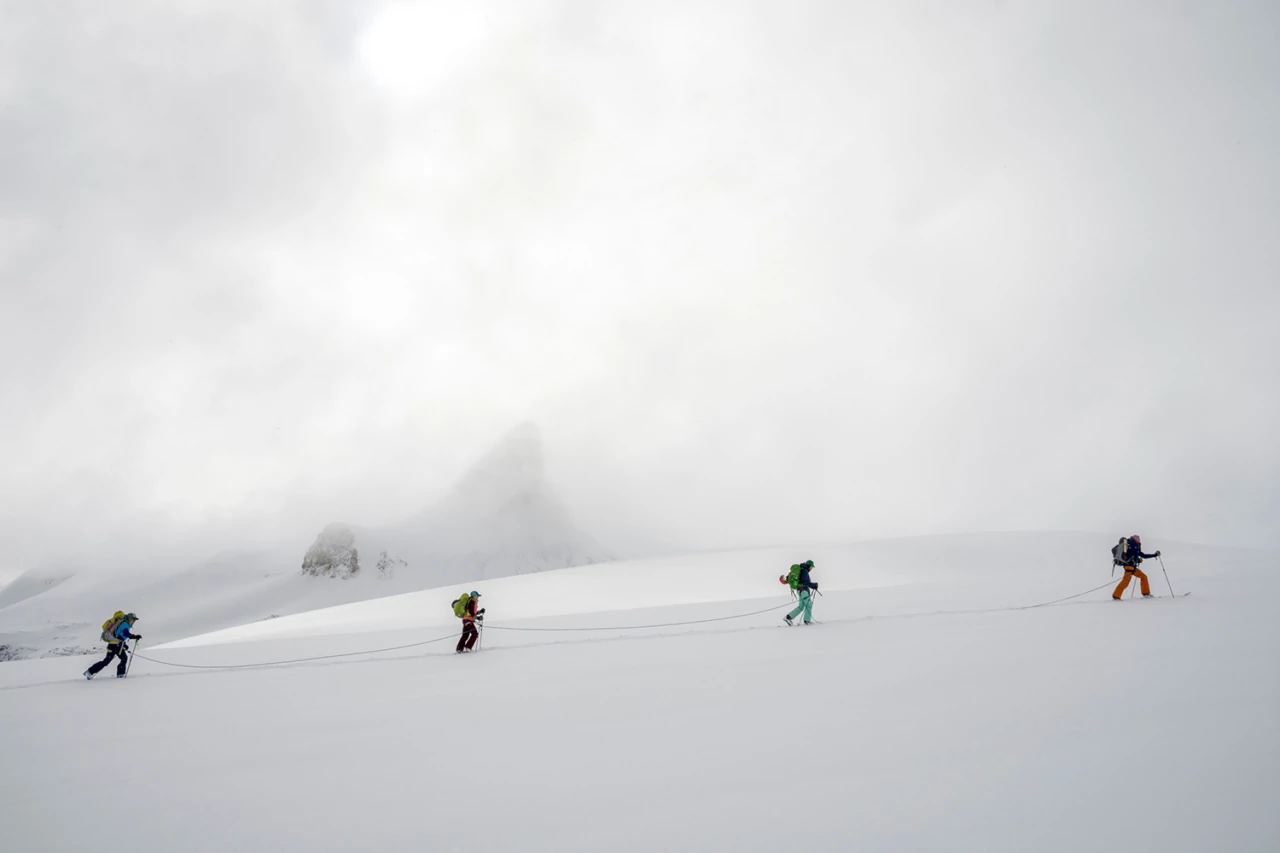Skiers roped together navigating a glacier in low-visibility alpine conditions - Rando Verbier